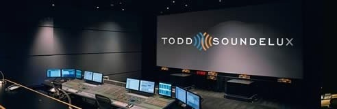 A dark sound mixing studio featuring a large projection screen with the Todd-AO Soundelux logo and multiple monitors.