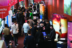Crowd of people interacting at an indoor event with colorful banners and information booths.