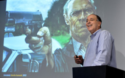 Man speaking at podium with projected image of a man aiming a handgun.